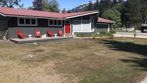 A two-story building with a red roof and a covered patio area with red chairs and a small table. - Cozy home next to airport with fenced backyard and lots of sun! (Juneau)