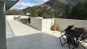 Eine Terrasse mit Blick auf eine gebirgige Landschaft, mit einem Blumentopf und Gartenmöbeln.