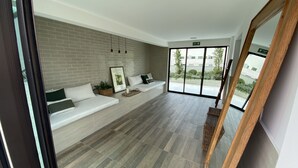 Ein geräumiger Raum mit einer langen weißen Couch, einer Ziegelwand, einem großen Fenster und einem Holzboden.
