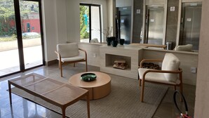 Ein modernes, gut beleuchtetes Zimmer mit einem großen Fenster, zwei weißen Stühlen, einem runden Holztisch und einem kleinen Holzschrank.