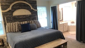 A bedroom with a large bed, a wooden bench, a stone accent wall, and a bathroom visible through an open door. - one level brick home with pet friendly fenced back yard , close to Chattanooga  (Ooltewah)