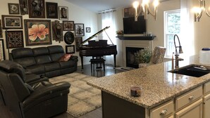 A living room with a black leather sofa, a grand piano, and a fireplace. - one level brick home with pet friendly fenced back yard , close to Chattanooga  (Ooltewah)