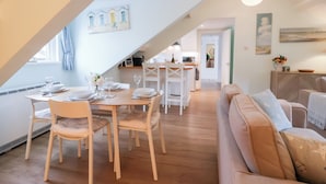 Ein Essbereich mit Tisch für vier Personen, eine Küche im Hintergrund und eine Wohnbereich mit einer Couch.