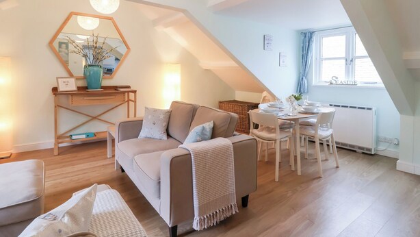 Ein gemütlicher Loft-Raum mit hohen Decken, einem Essbereich mit Tisch und Stühlen, einer Couch mit Kissen, einem Holzkonsolentisch und einem großen Spiegel.