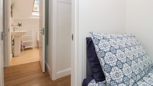 Ein Zimmer mit Holzboden, einer weißen Tür, einem blauen und weißen Kissenmuster und Blick in ein Badezimmer mit Waschbecken und einer Meerstern-Dekoration.
