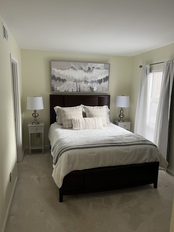 A bedroom with a large bed, two bedside tables, a headboard, and a window with curtains.