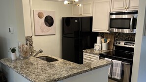 A kitchen with a granite countertop, stainless steel appliances, and white cabinetry. - Charming Pinehurst Golf Front Condo (Pinehurst)