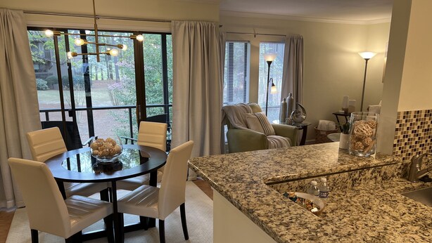 A modern kitchen with granite countertops, a dining area with a glass table, and a cozy seating area with a green armchair. - Charming Pinehurst Golf Front Condo (Pinehurst)