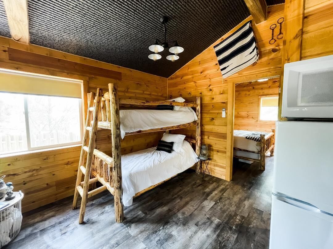 A cabin with three bunk beds, a refrigerator, and a wooden interior.