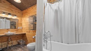 Une salle de bain de style rustique, avec des murs en bois, une baignoire, un lavabo et des toilettes.