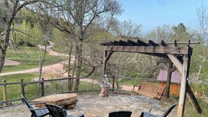Un espace extérieur aménagé avec un coin salon, une pergola, un foyer en pierre et des chaises.