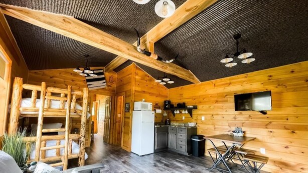 Un intérieur de chalet chaleureux, avec un revêtement en bois, un coin cuisine et un espace salon comprenant un canapé et une table à manger.