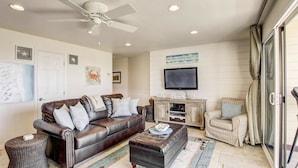 A living room with a brown leather sofa, a coffee table, a television, and a ceiling fan. - Ocean Front View - Steps from the beach! (San Diego)