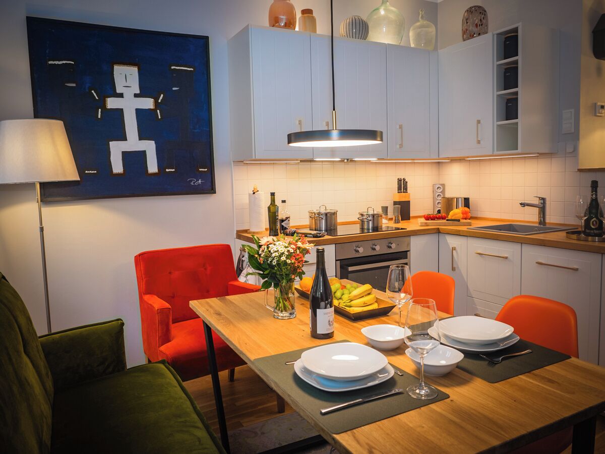 A modern kitchen with white cabinets, a wooden dining table set for two, and a red chair.
