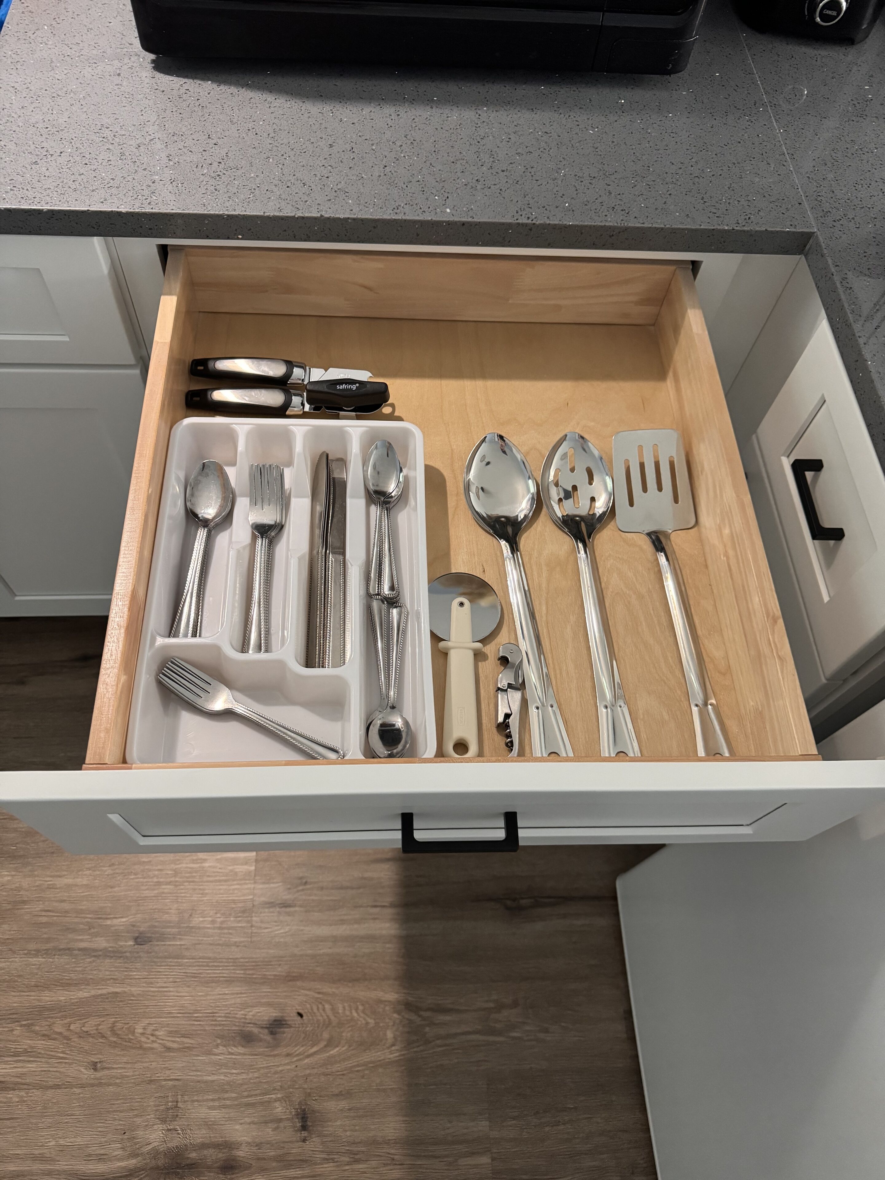 Un tiroir contenant un ensemble de couverts, notamment des fourchettes, des couteaux, des cuillères et une spatule.