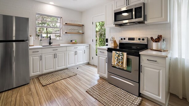 Una cocina moderna con armarios blancos, electrodomésticos de acero inoxidable y una ventana con vistas a zonas verdes.