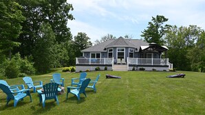 A house with a porch and a lawn with blue chairs. - Luxury Cottage in Alex Bay 3 bedrooms, 2.5 baths.  Book your 2026 Vacation Now!! (Alexandria Bay)