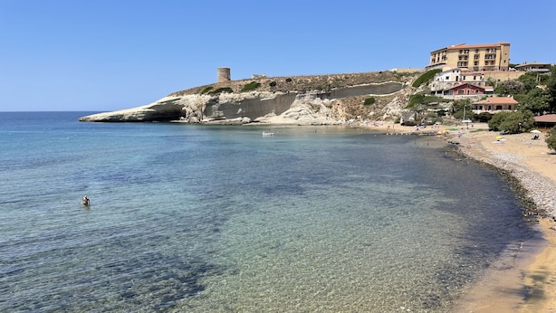 Une zone côti ère caractérisée par des eaux limpides, une plage de sable et un bâtiment situé sur une colline.