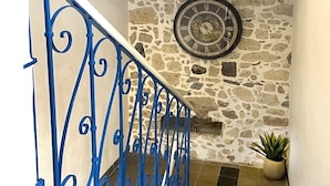 Un escalier avec des rampes en métal bleu, un mur en pierre orné d’une horloge et une plante en pot.