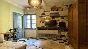 Un salon chaleureux avec un mur en pierre, un meuble en bois, un canapé, une table et un téléviseur fixé au mur.