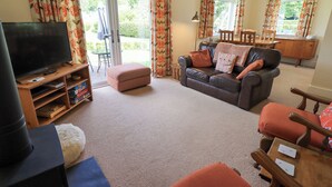 A living room with a television, sofa, ottoman, and a dining area with chairs and a table. - Limhus Cottage (Keswick)