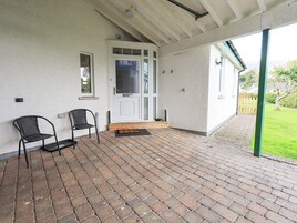 A covered patio with two black chairs, a white door, and a brick floor.