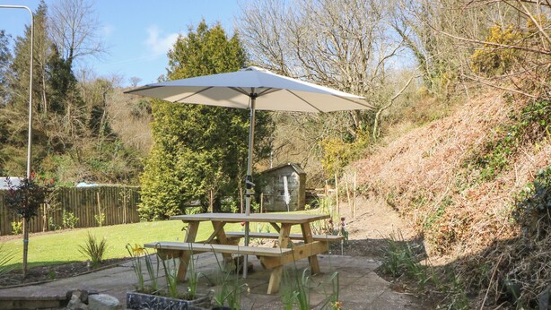 A patio with a wooden table and bench, an umbrella, and a small shed. - 1 Closheen Lane (Rosscarbery)