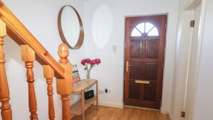A wooden staircase, a mirror, a door with a semi-circular window, and a small table with a vase of flowers. - 1 Closheen Lane (Rosscarbery)