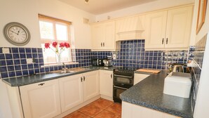 A kitchen with white cabinets, a black stove, and a blue tiled backsplash. - 1 Closheen Lane (Rosscarbery)