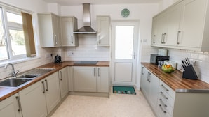 A modern kitchen with light-colored cabinets, a stainless steel range hood, a sink, and a microwave. - 53 St. Brides View (Haverfordwest)