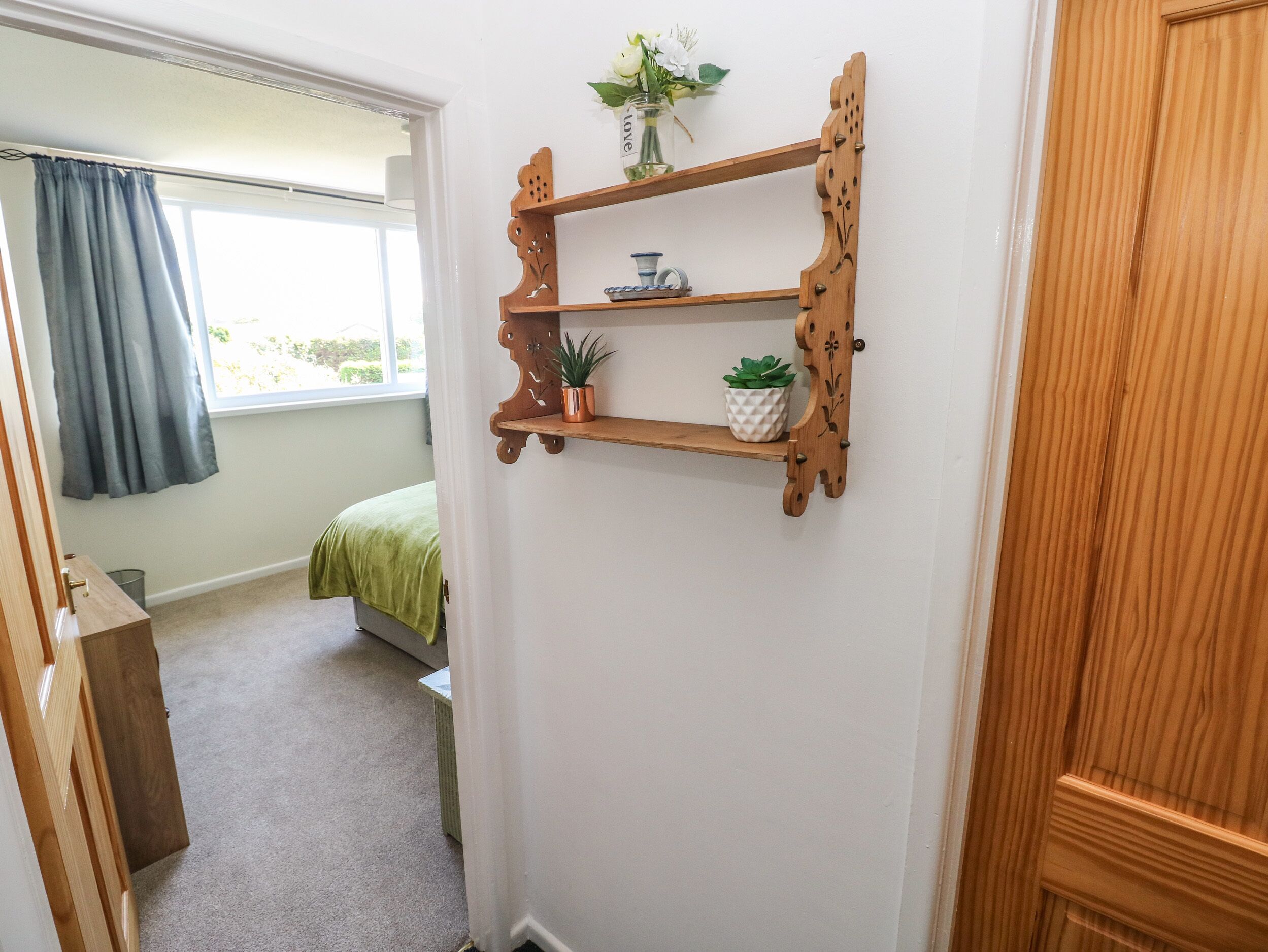 Une pièce avec une étagère en bois adossée au mur, sur laquelle sont posés un pot de fleurs et un petit objet décoratif.