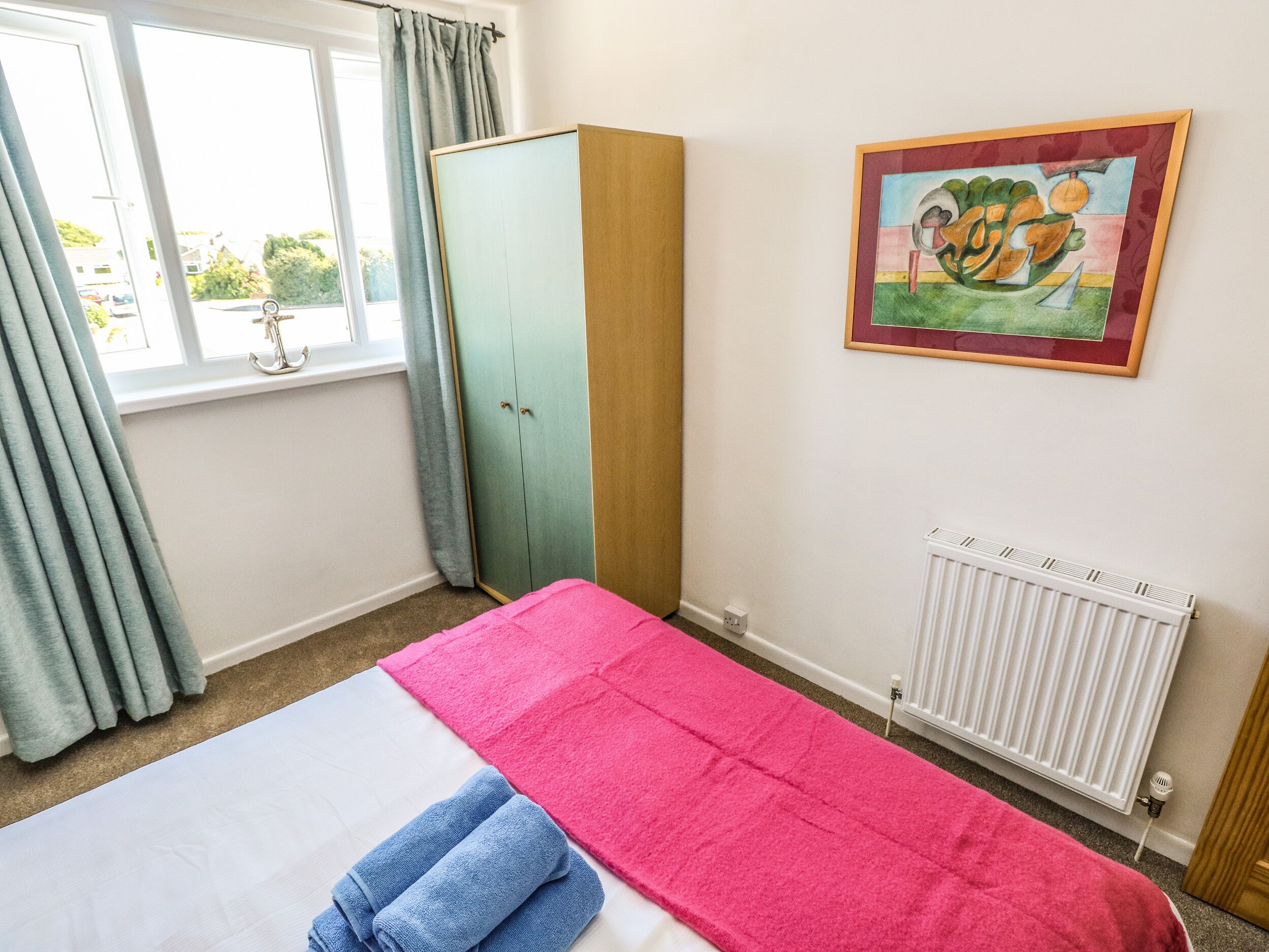 Un dormitorio con cama, armario, radiador y ventana con cortinas.