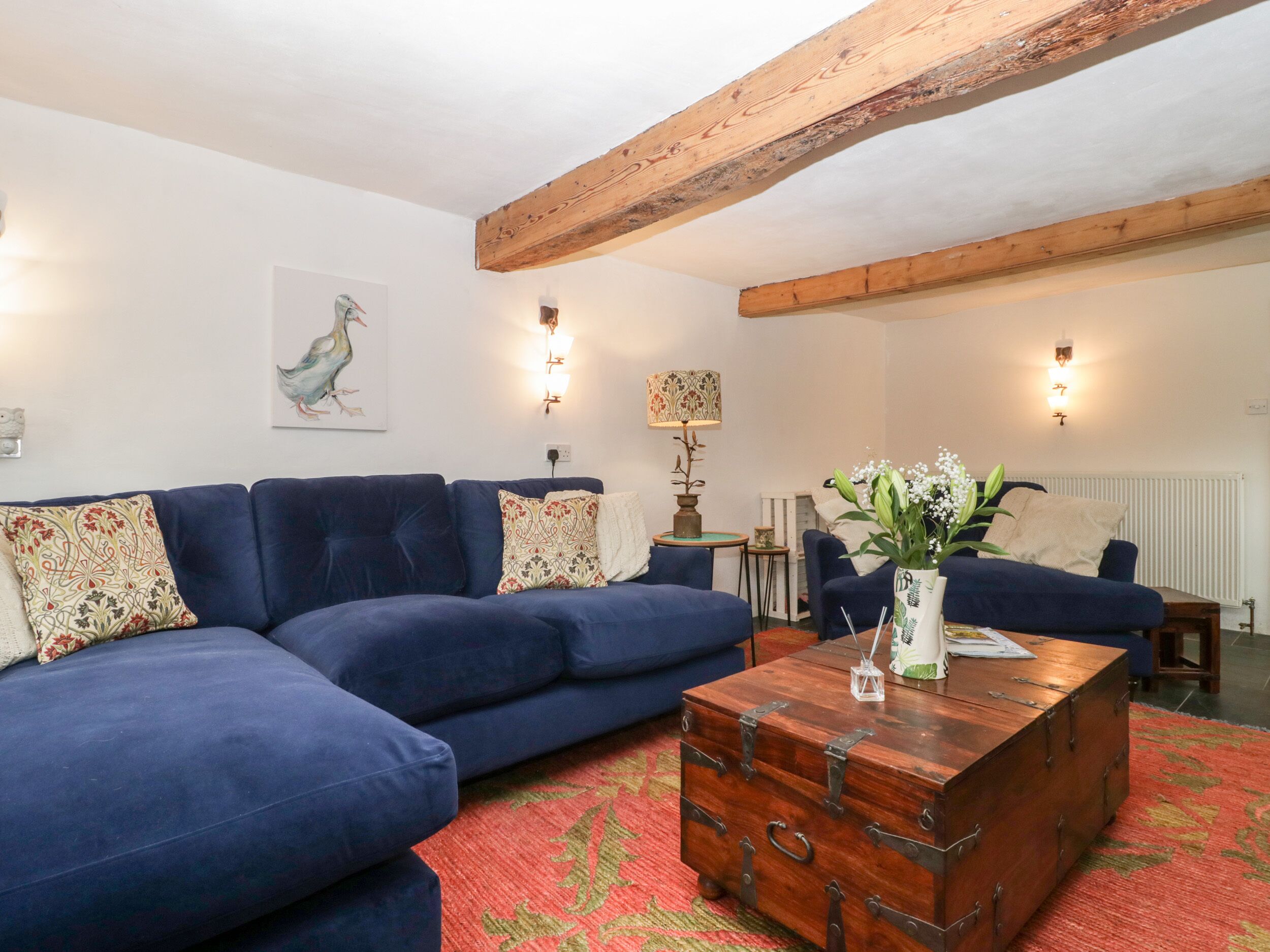A living room with a blue sofa, a wooden chest, and a red patterned rug.