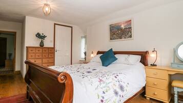 A bedroom with a wooden bed, a nightstand with a lamp, a dresser, and a painting on the wall.
