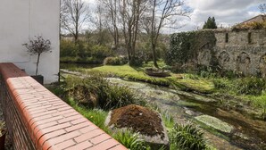 Een tuin aan de rivier met een pad van baksteen, een klein bootje en een stenen muur.