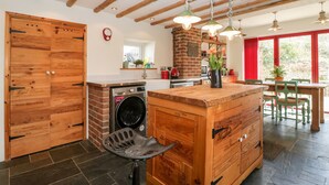 Een keuken met houten kastjes, een ingebouwde wasmachine, een eethoek met een tafel en stoelen, en een rood gordijn.