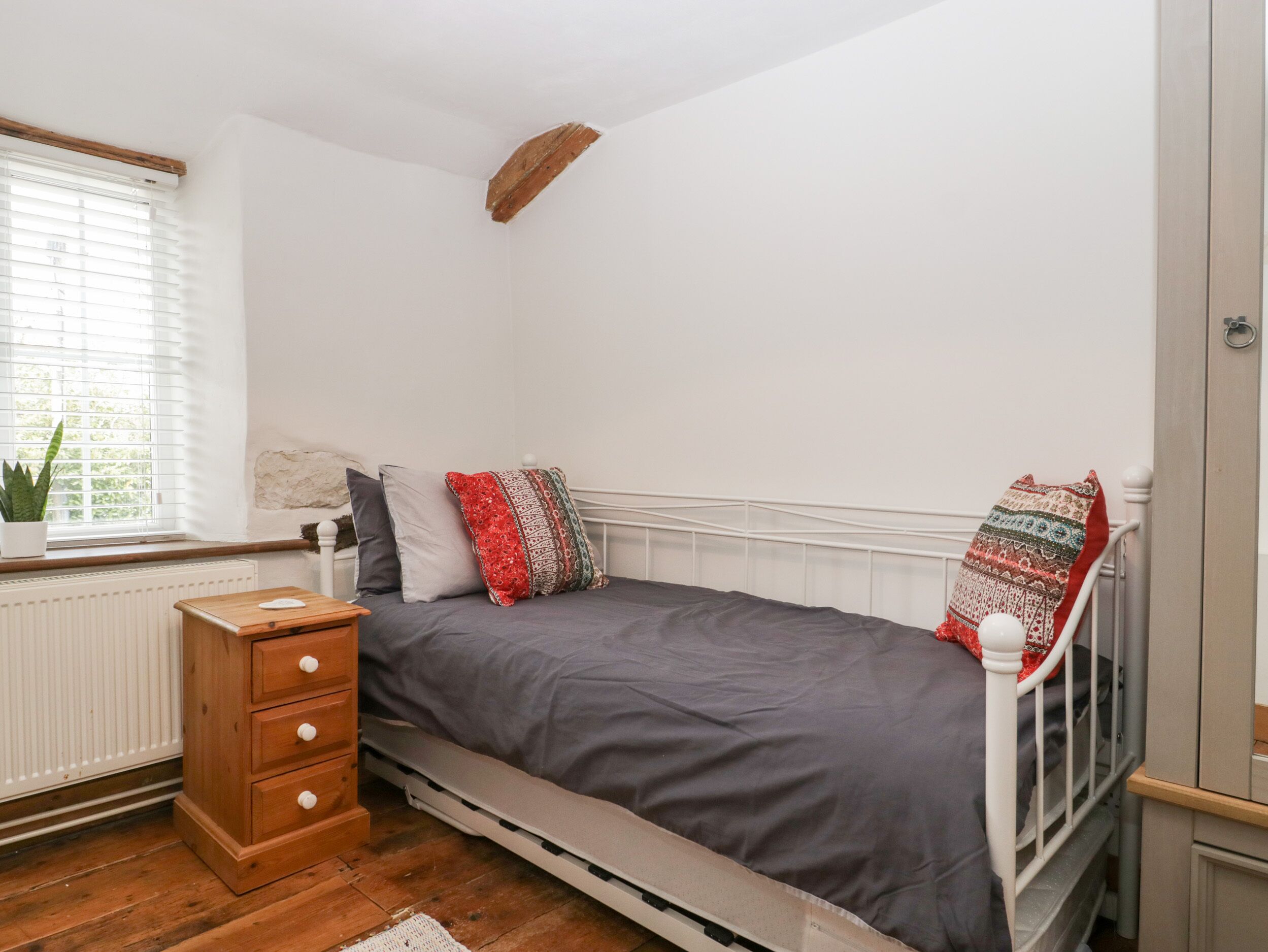 Une chambre à coucher avec un lit, une table de chevet en bois, un radiateur et une fenêtre avec des stores.