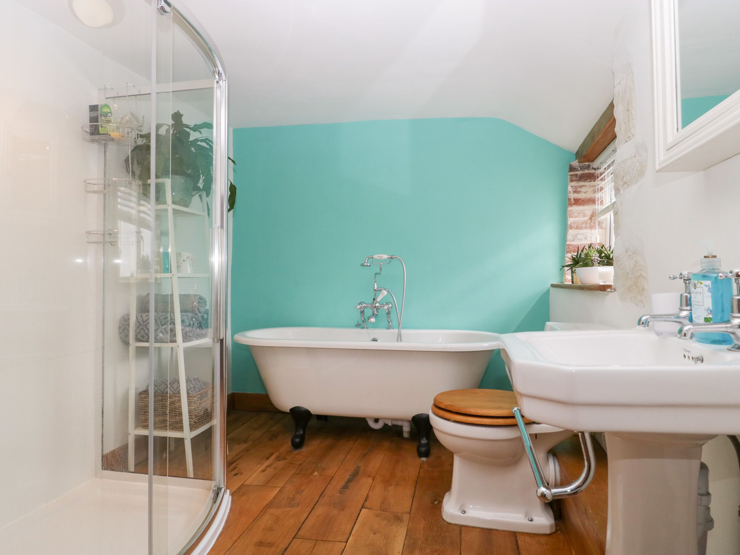 A bathroom with a glass shower enclosure, a freestanding bathtub, and a toilet with a wooden seat.