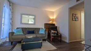 A living room with a sofa, armchair, and a small table with a suitcase.