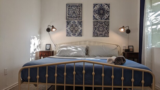 Ein Bett mit Kopfteil, zwei Nachttische mit Lampen und vier dekorative Wandfliesen.