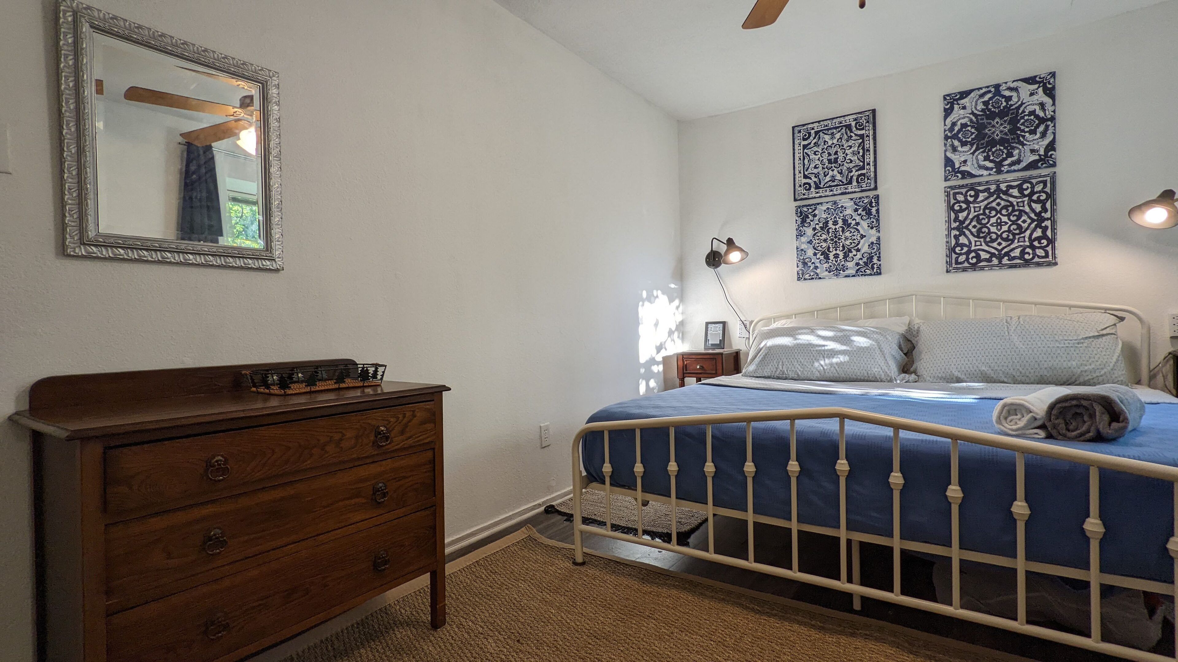 Une chambre avec une commode en bois, un cadre de lit en métal et des décorations murales à motifs.