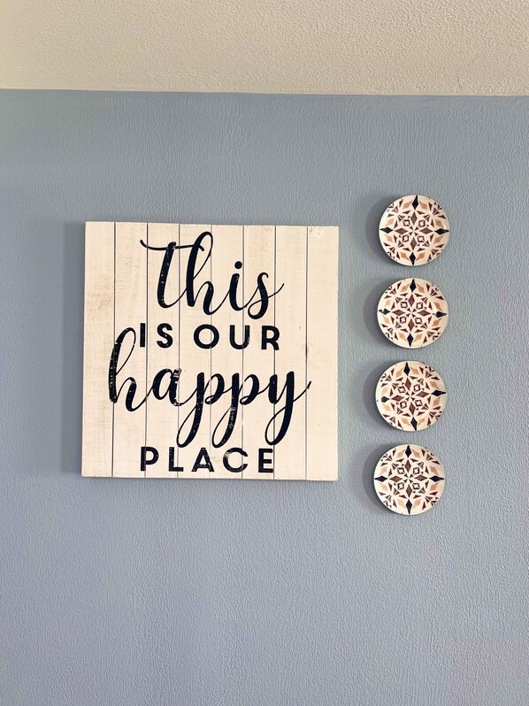 Et træskilt med teksten 'this is our happy place' og fire dekorative tallerkener med geometriske mønstre.
