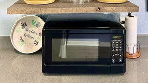 A kitchen counter with a microwave, yellow dishes, a sign, and decorative items. - The Mark at Surfside, Apt. 9 (Surfside Beach)