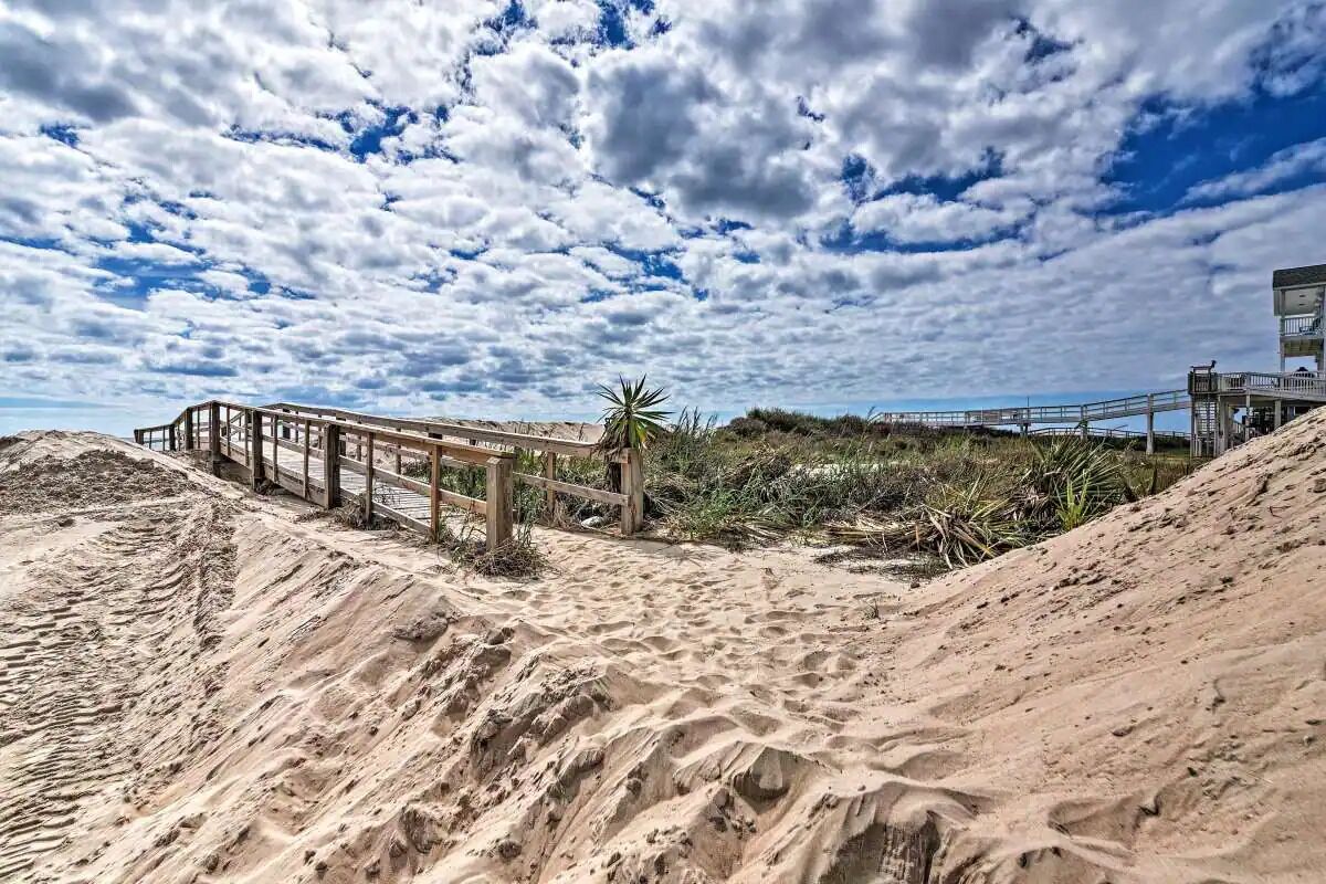 Una playa arenosa con un pasarelas de madera que lleva a una torre de salvavidas.