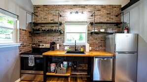 A kitchen with a brick wall, stainless steel appliances, wooden countertops, and a window.