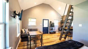 A loft-style living space with a dining area, a sofa, a staircase, and a kitchen area.