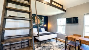 A bedroom with a loft bed, a ladder, a desk, and a window.
