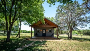 A small cabin with a porch, surrounded by trees and a fenced yard.