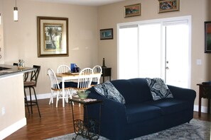 Ein Wohnzimmer mit einem dunkelblauen Sofa, weißen Stühlen, einem kleinen Tisch und einer Küchenzeile mit Esstisch und Stühlen.