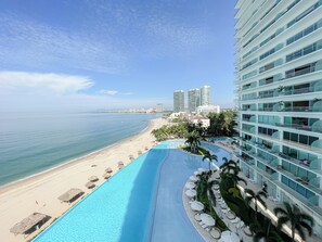 A resort with a pool, beach, and high-rise buildings in the background. - Lujoso Peninsula T3 Frente al Mar (Puerto Vallarta)